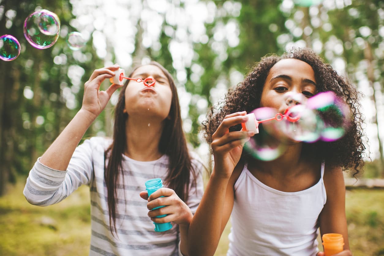 Two children blowing bubbles outdoors in the woods